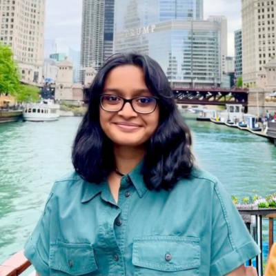 Vichar in front of the blue chicago river in downtown with a dark brown bridge in the background